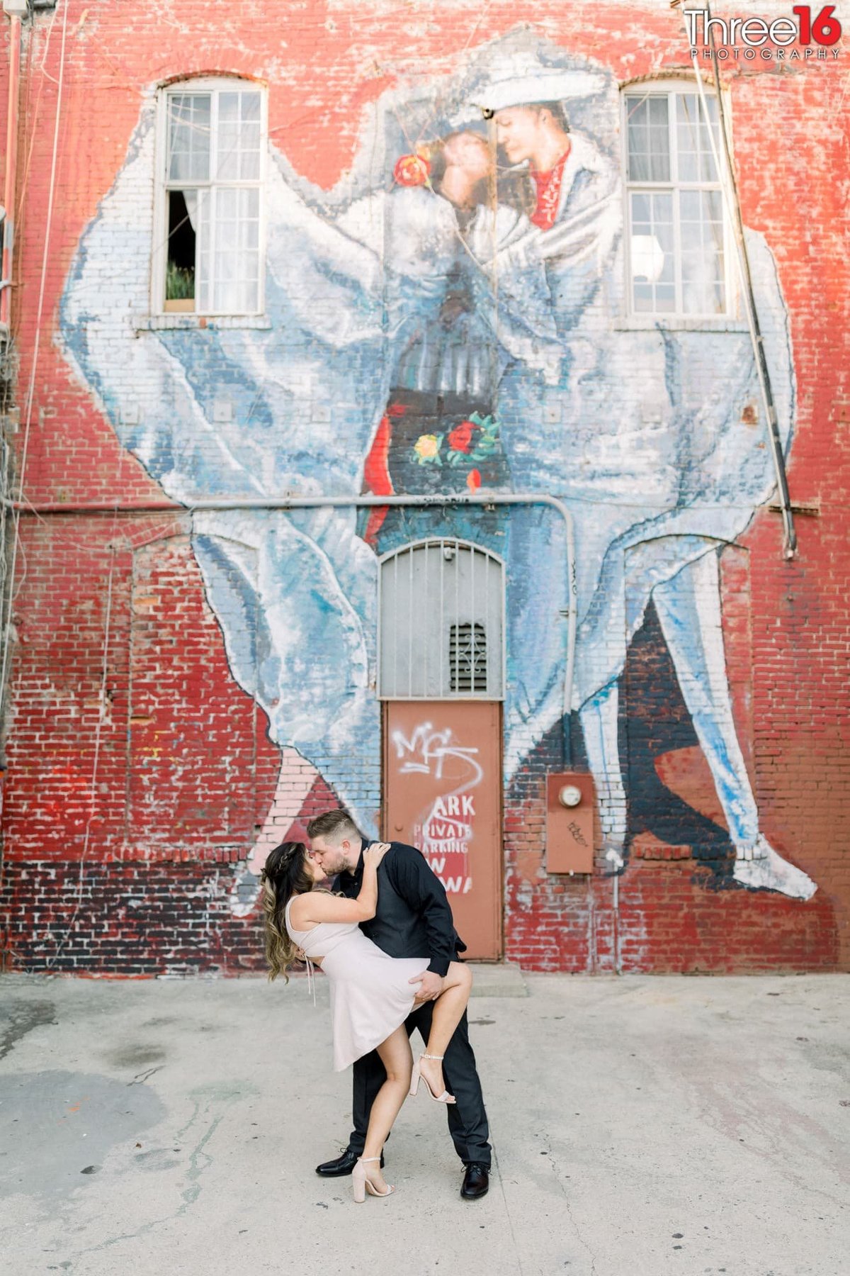 Groom to be dips and kisses his Bride in front of a mural depicting the same