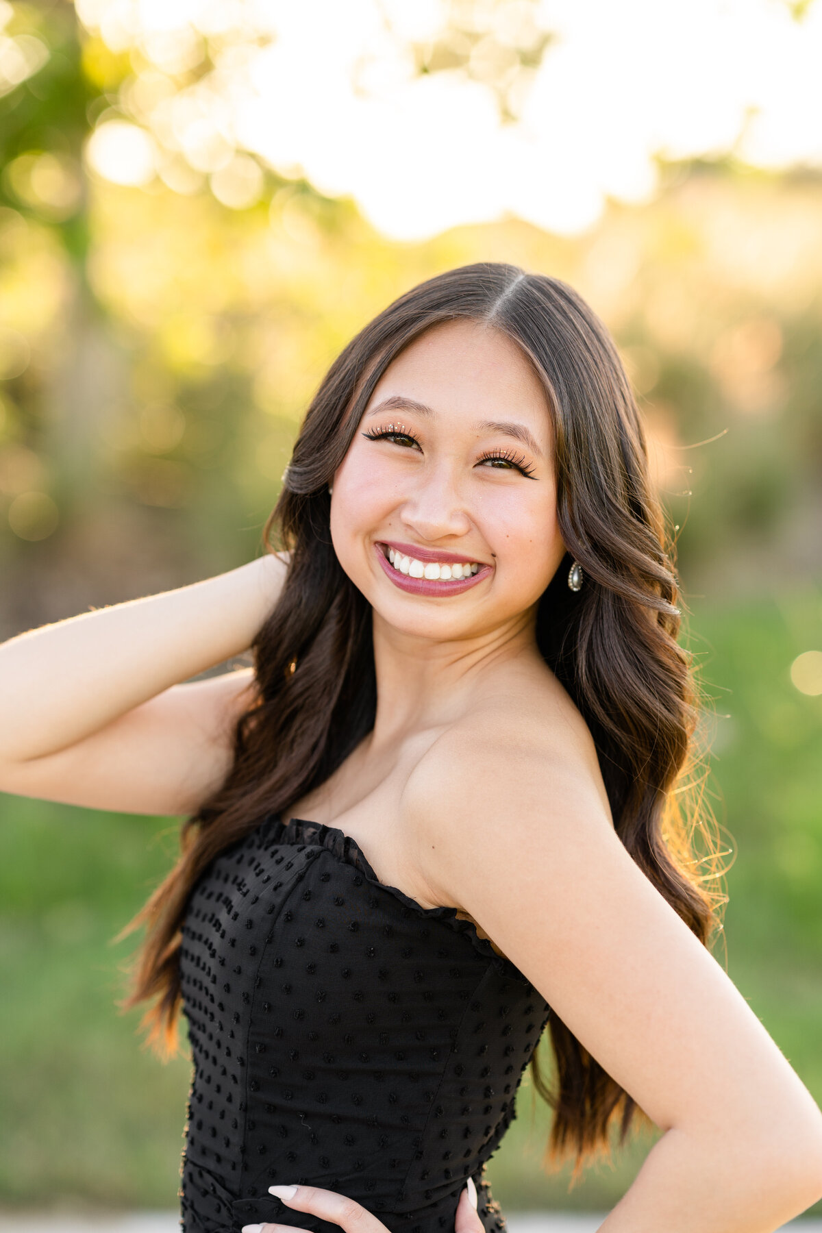 Houston High School senior girl smiling with hand on hip and in hair while wearing black dress at sunset at Josey Lake Park