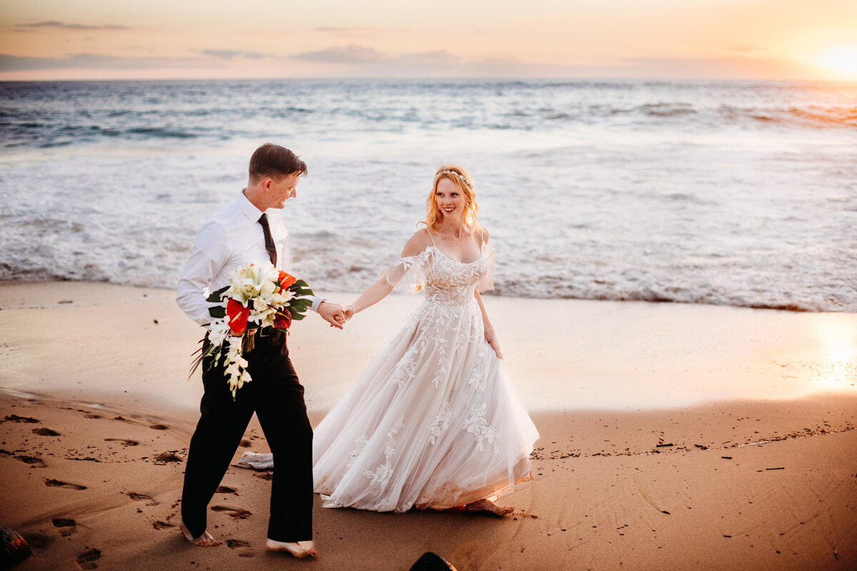 Bride and groom holding hands and walking along the beach