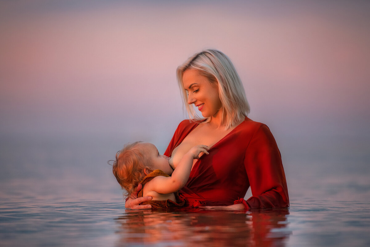 mother gazing into her baby's eyes while breastfeeding in the water with orange dress.