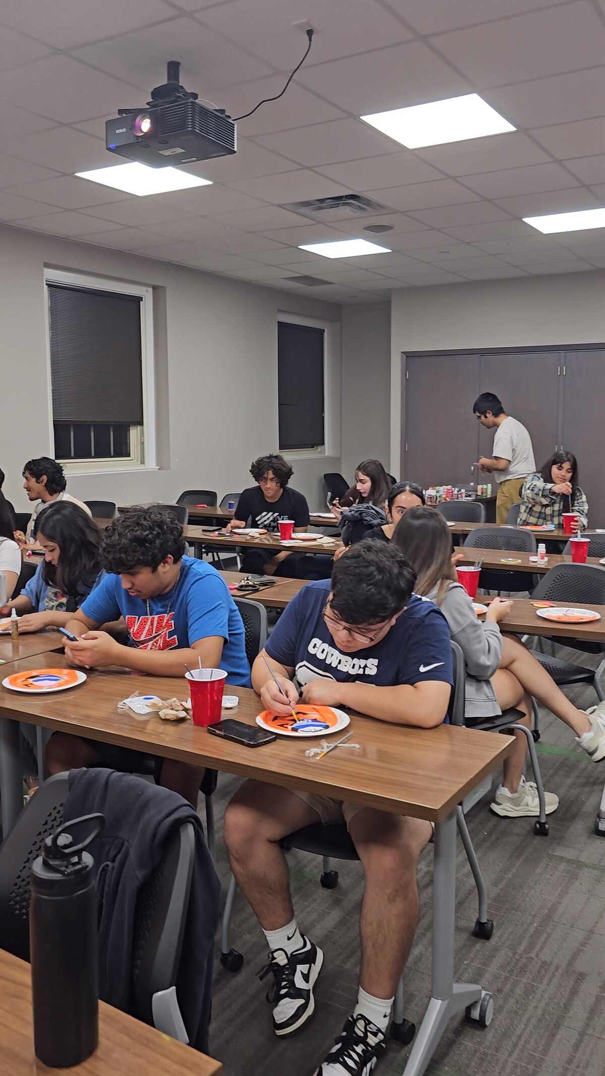 Soleil Vida Studio as a group of young individuals engages in our vibrant art workshop. Seated on plastic chairs around a giant wooden table, they paint their pieces with joy, using paints and brushes.