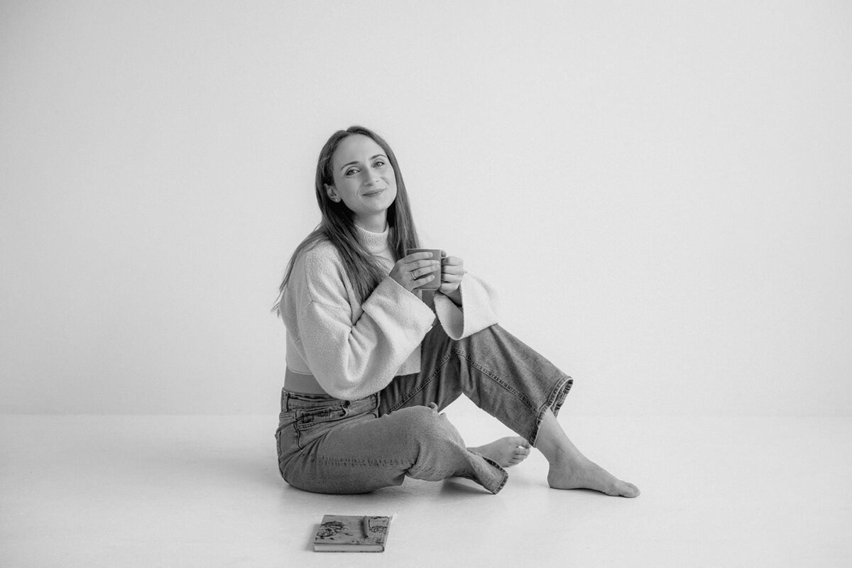Woman sitting on the floor with a cup of coffee in her hands.