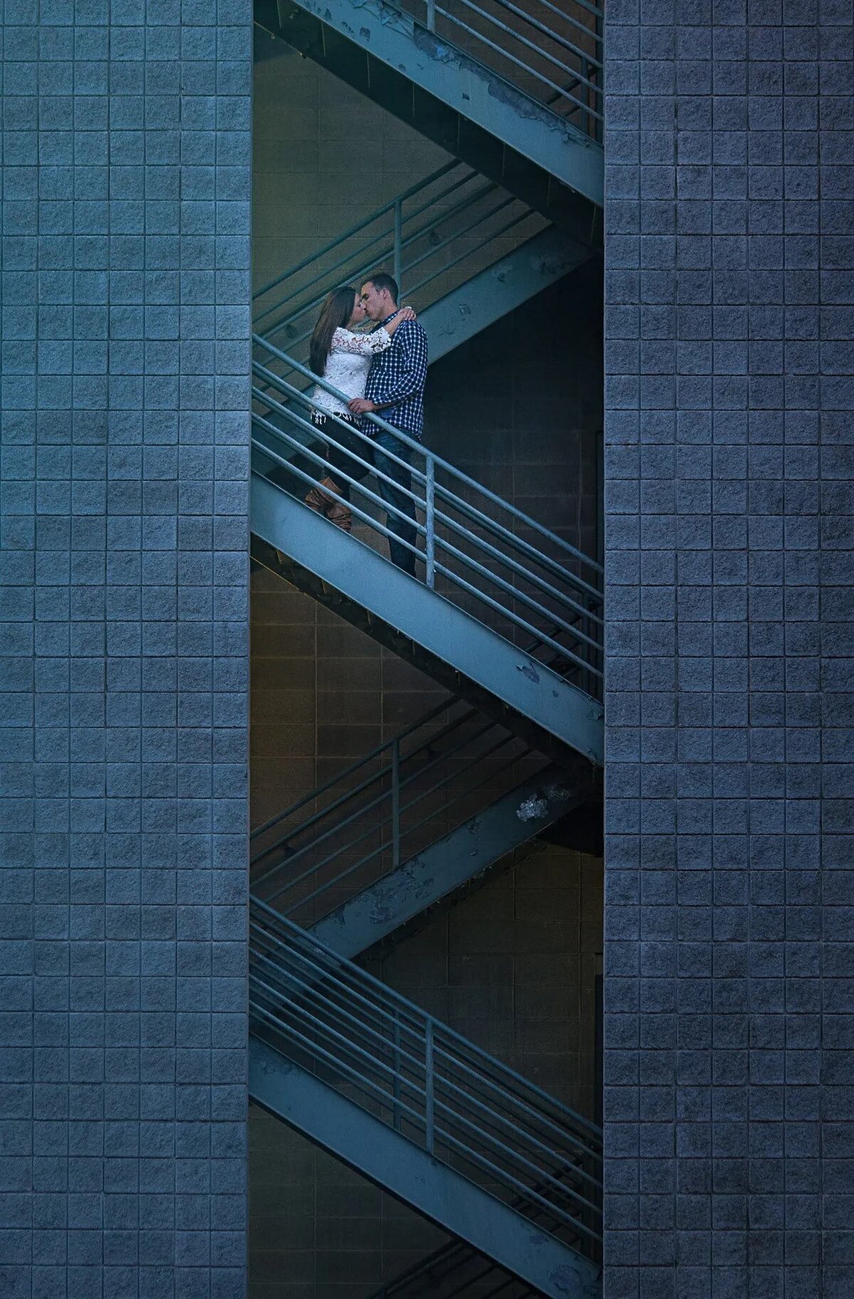 Couple sharing a moment on a staircase within a modern architectural structure, surrounded by large gray tiles