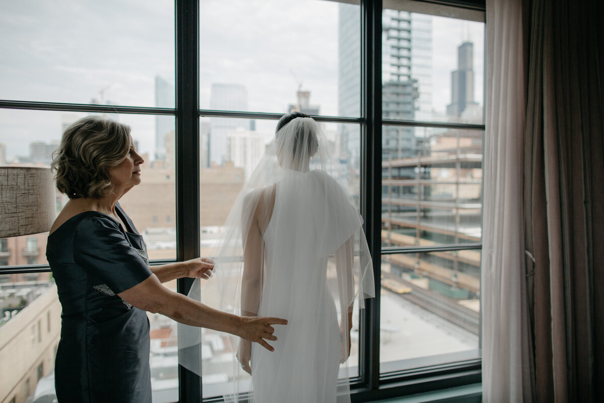 Bride looking at Chicago skyline while mother fixes veil