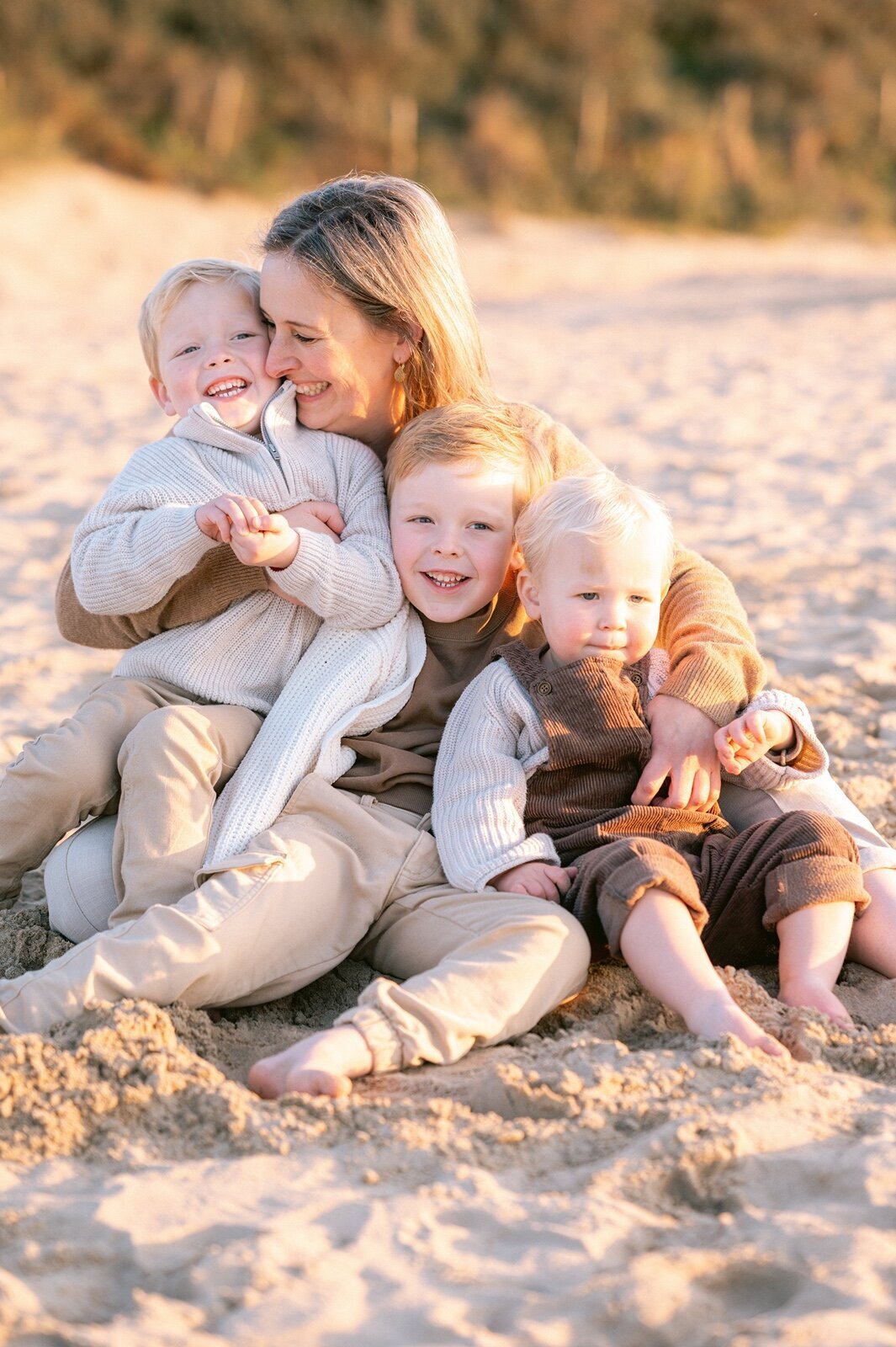 Moeder zit met haar drie zonen op het strand en knuffelen en lachen