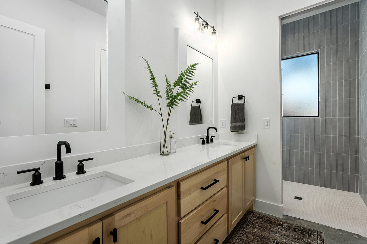 double vanity with white countertops and wood cabinets, large shower with gray tile