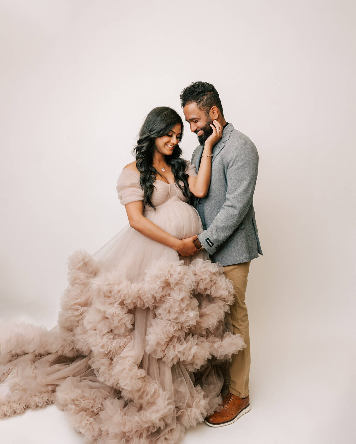 maternity portrait of husband and wife. Both have their hand on her belly and are smiling down at their baby in her tummy.