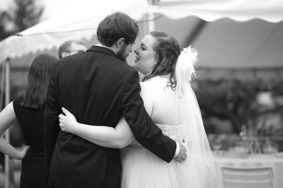 Elegant black and white photo capturing a tender moment between a bride and groom from behind. The bride has her arms around the groom and is whispering in his ear, showcasing their intimate connection on their special day in Salem, Oregon.