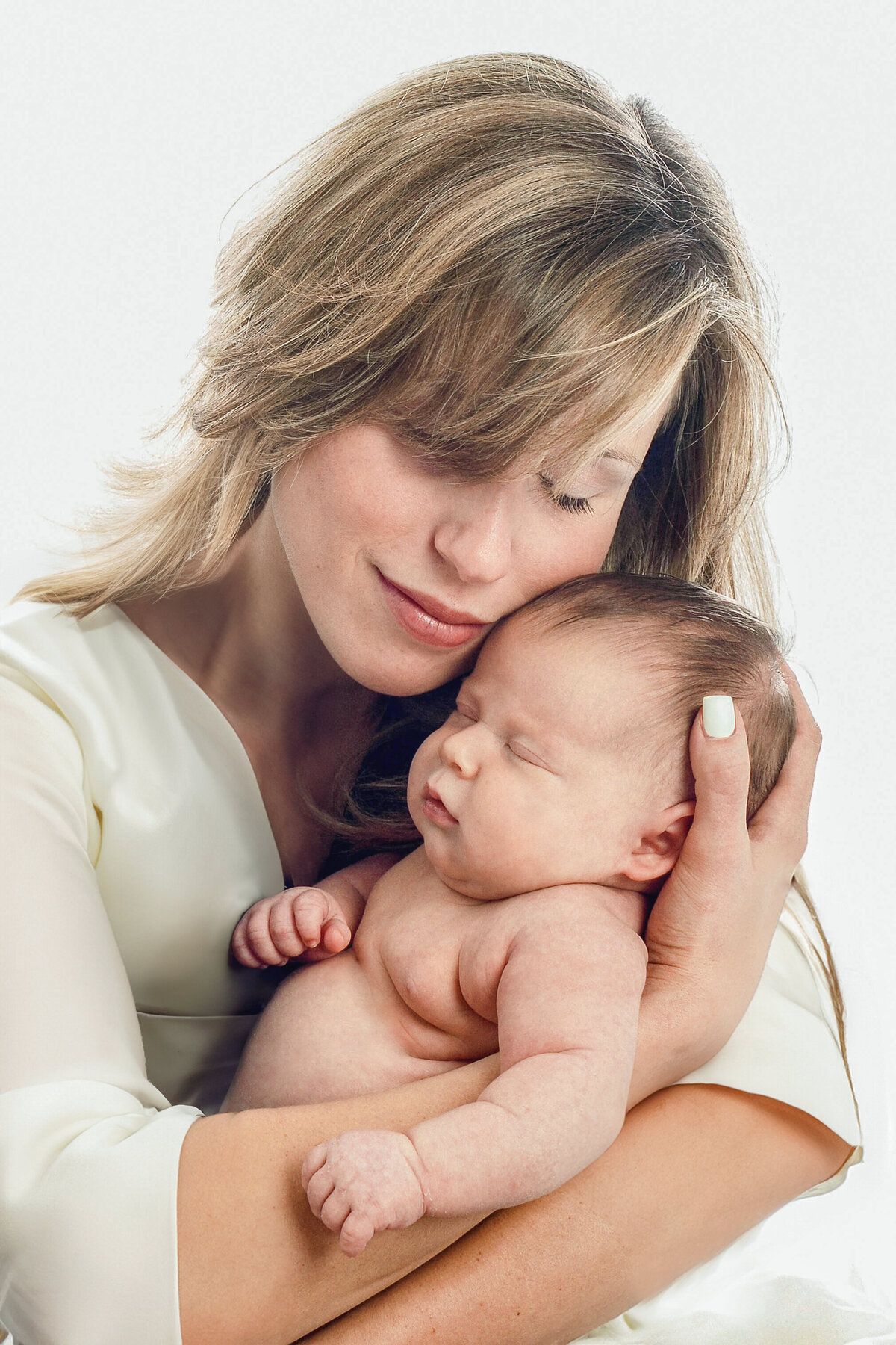 An adorable baby being held in  his mom's arms on a white backdrop.