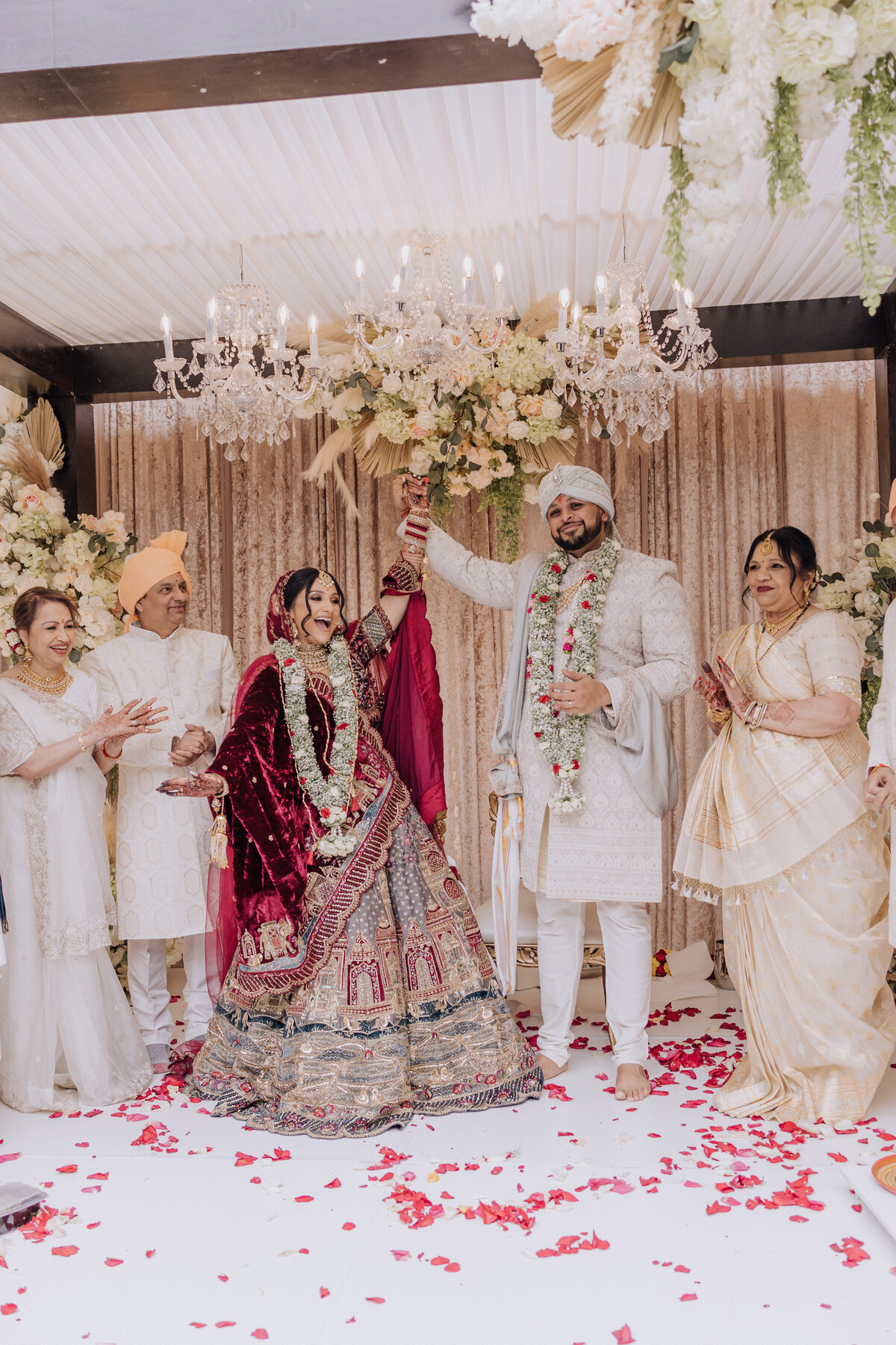 Hindu wedding ceremony moment with bride and groom celebrating beneath a floral mandap surrounded by family.