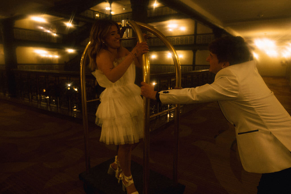 A person pushing their partner on a luggage cart