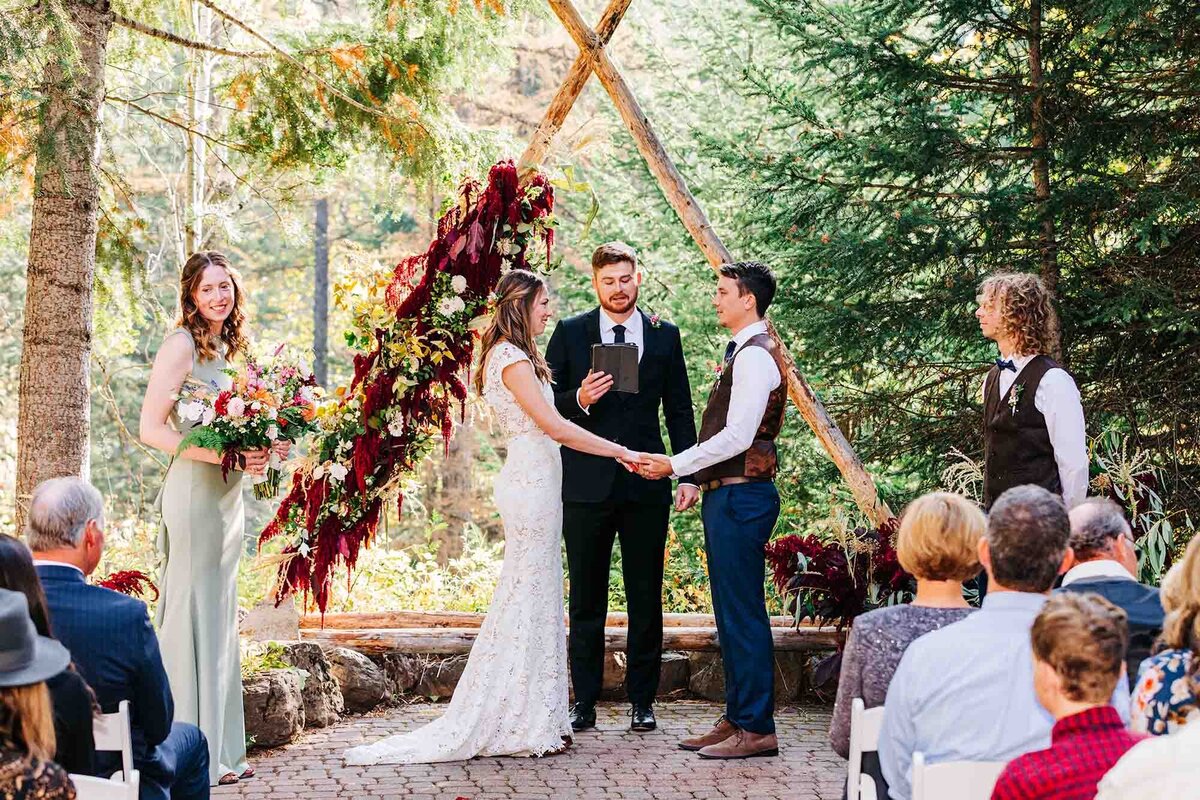 Bride and groom holding hands at flower arch, Izaak Walton Inn, Essex, MT