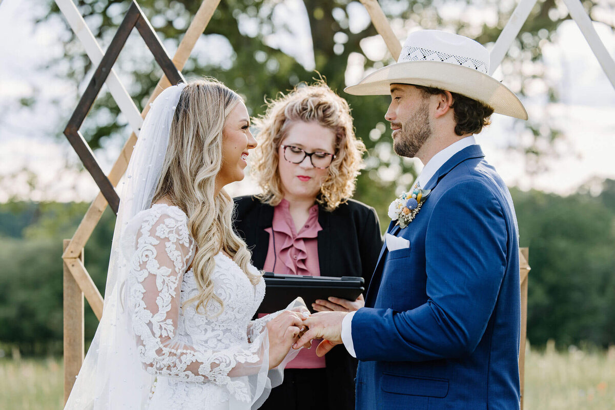 bride placing wedding ring on groom's finger during wedding day vow exchange  at alter