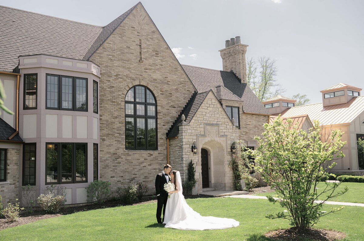 A couple poses for their wedding photo in the front of a manor in Grand Rapids