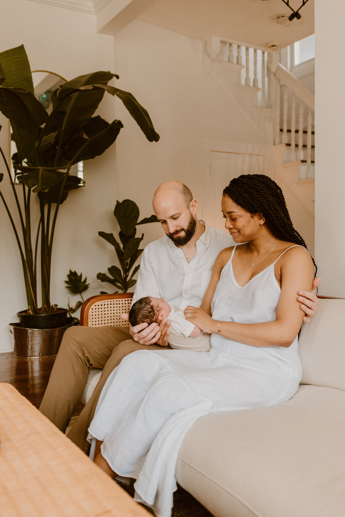 Hudson Valley Newborn Photographer captures a cozy scene of parents seated on a couch, cradling their baby.