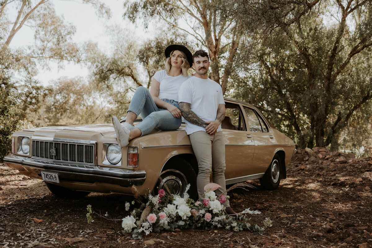 couples engagement session sitting on top of a holden car