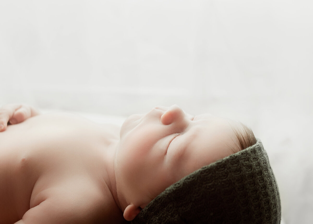 Newborn baby boy, wearing green hat during newborn photoshoot in Franklin Tennessee photography studio