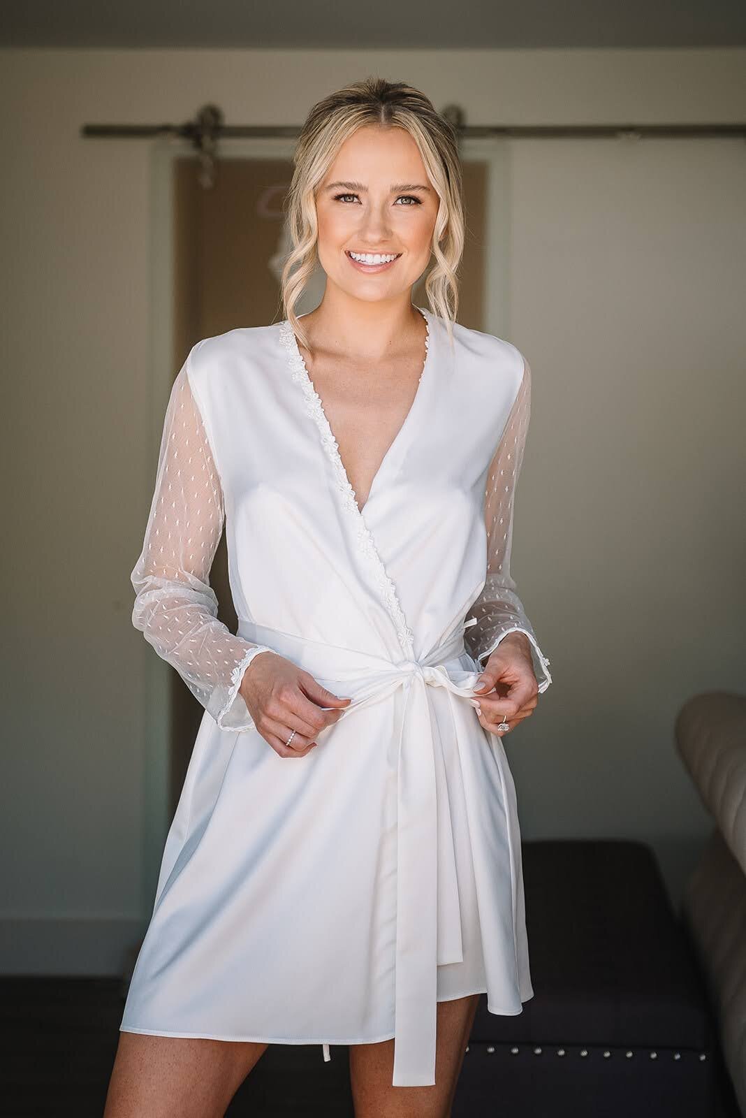 Bride poses in her white satin robe  on her wedding day.