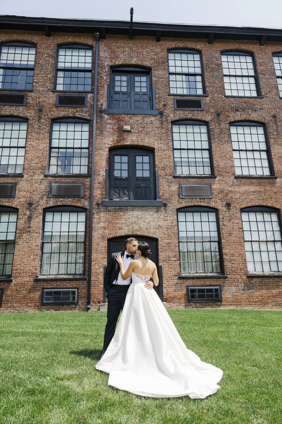 Bride and groom pose outside of The Roundhouse with the lawn and hotel as the background