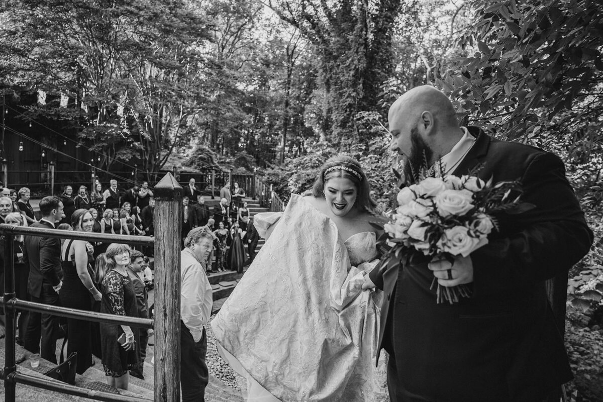 A newlywed couple walking together as one holds up their wedding dress 