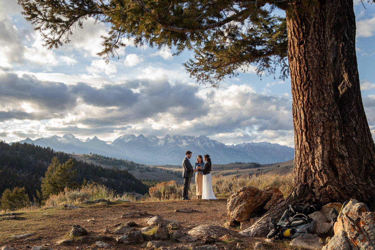 An officiant reads during a Wyoming elopement ceremony while the bride and groom stand facing each other and holding hands.