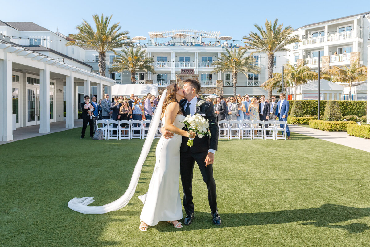 The bride and groom share a celebratory kiss after their wedding ceremony at Lido House, with guests cheering in the background