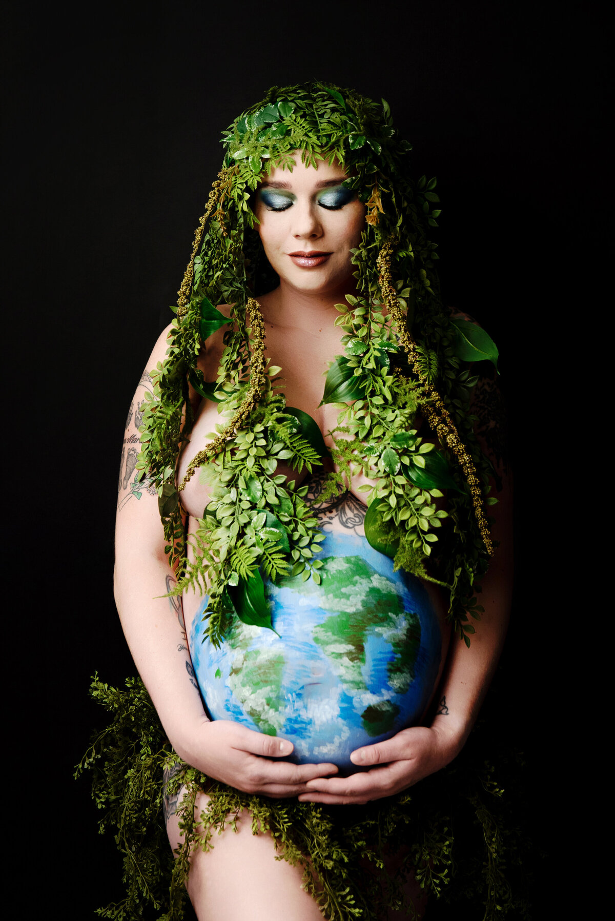 st-louis-maternity-photographer-pregnant-mom-holding-belly-painted-as-earth-posing-as-mother-earth-with-greenery-surrounding-her