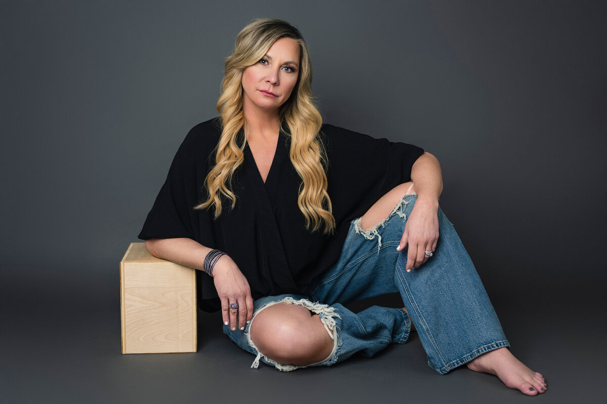 Woman in a black top and ripped jeans, sitting casually with one knee up captured by Leslie Q Photography