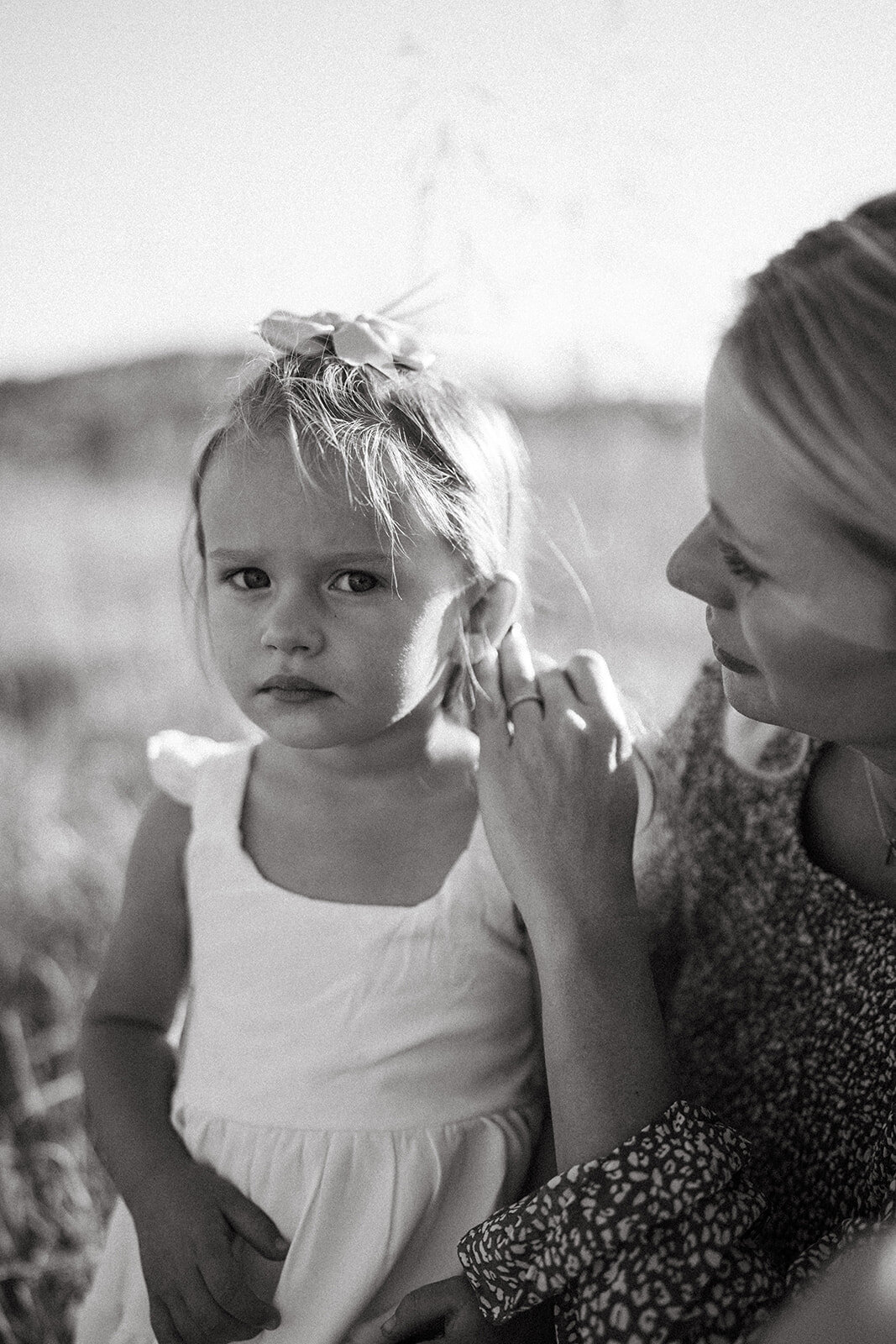 Little girl with a puzzled look as her mom brushes hair from her face during a lifestyle family session