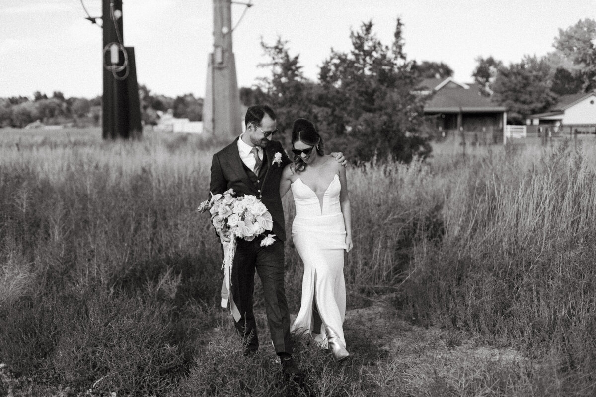 bride and groom looking down and walking towards camera in tall grass