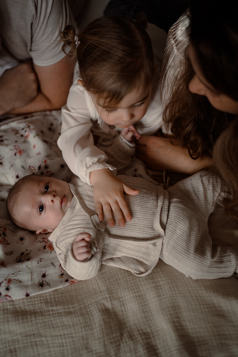 Zus aait haar baby zusje over haar buik tijdens een newbornshoot in Apeldoorn