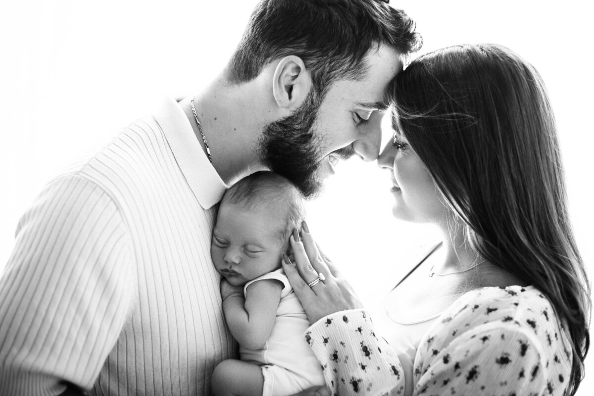 Black-and-white photo of a young couple sharing an intimate moment with their newborn baby