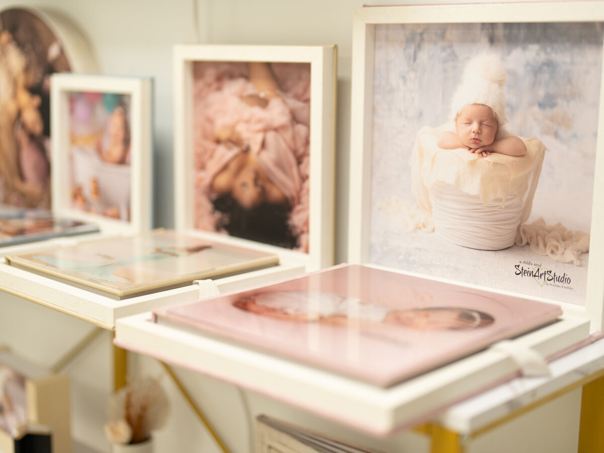 Framed baby photos on display; one features a sleeping infant in a fluffy white hat. Soft background tones create a serene, tender atmosphere.