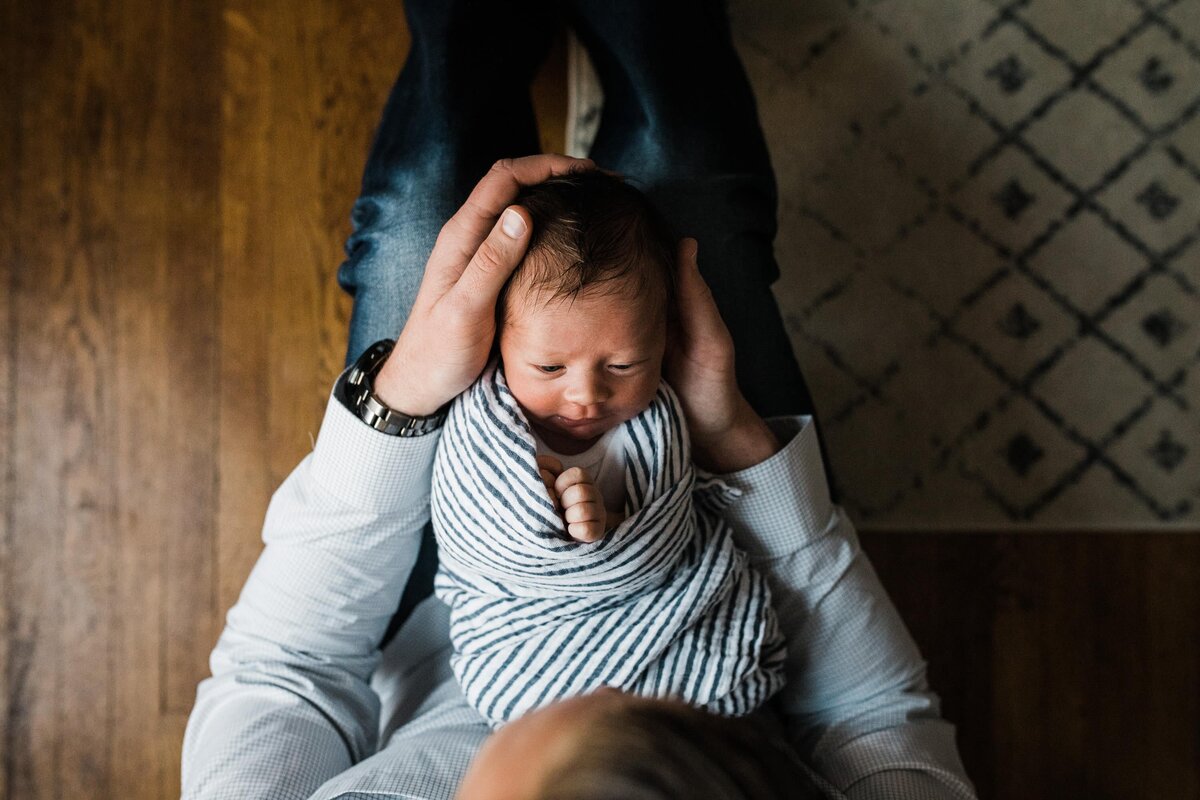 A parent holding a newborn baby while sitting on a wooden floor for their home newborn photography session.