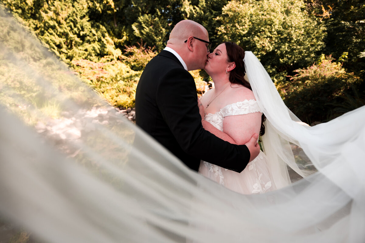 couple kiss in the background as the brides veil swoops around them