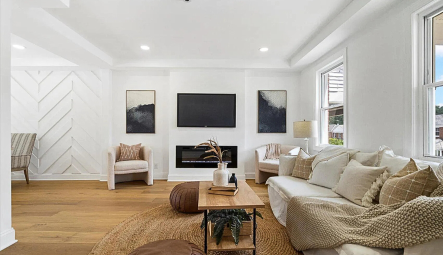 Beautifully renovated living room featuring a modern fireplace with wall-mounted TV, custom trim work, wide-plank hardwood floors, and natural light—designed for comfort and style.