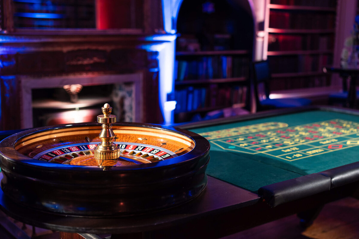 roulette wheel and table in avington park’s library which is washed in blue lighting for a casino night party planned by westacott weddings and events