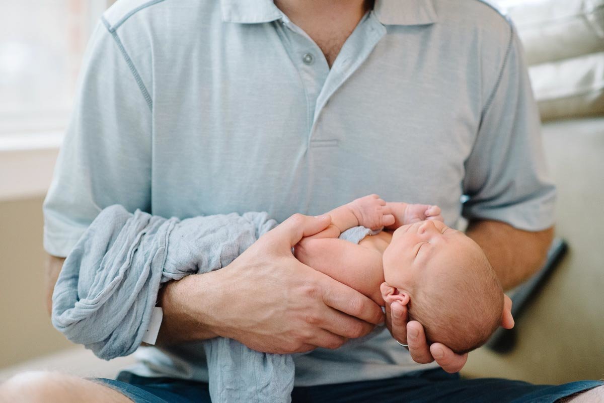dad in grey shirt hold newborn sons head in his hand