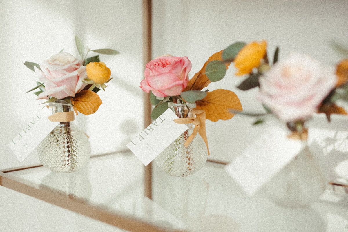White place cards with light gray font tied to glass vases filled with flowers.