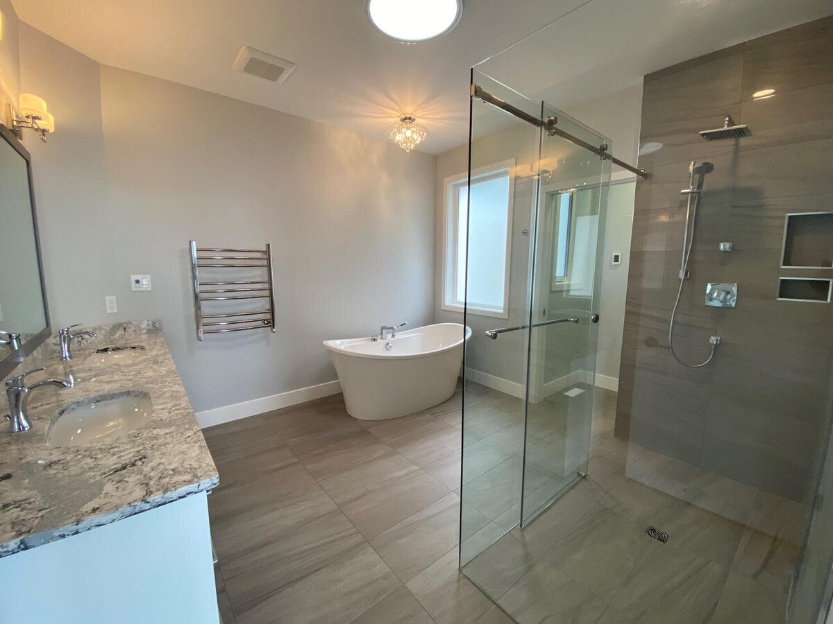 Custom bathroom design with gray tile floors, freestanding bathtub with chandelier above.
