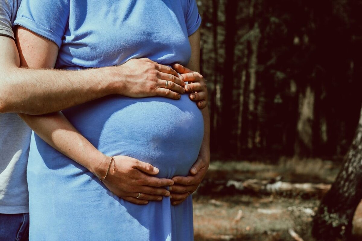 Een close-up van de handen van aanstaande ouders die de buik van de zwangere vrouw vasthouden, met een natuurlijk landschap op de achtergrond