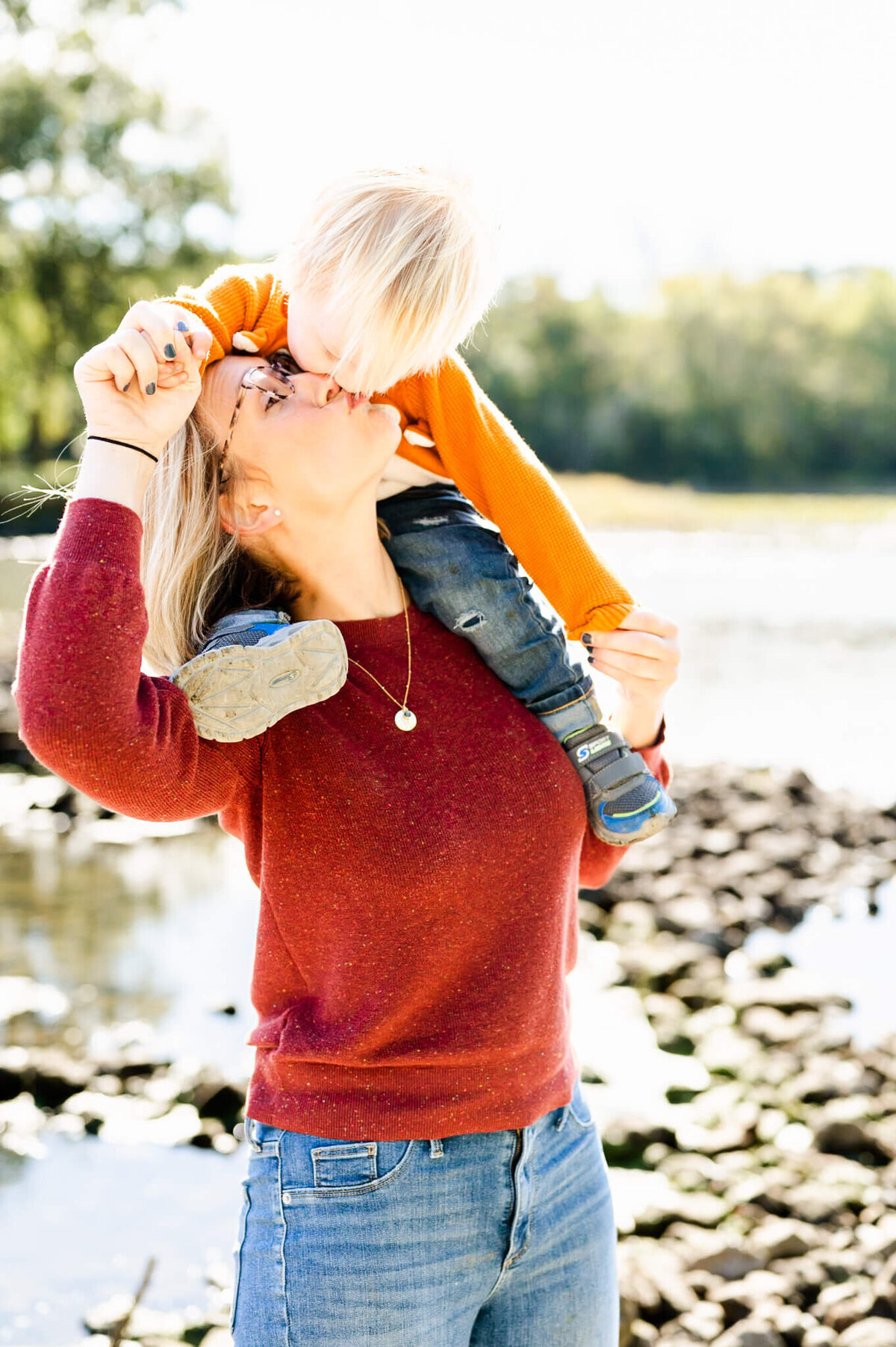 Mom kissing toddler boy on shoulders at Fabyan Forest Preserve in Geneva, IL.