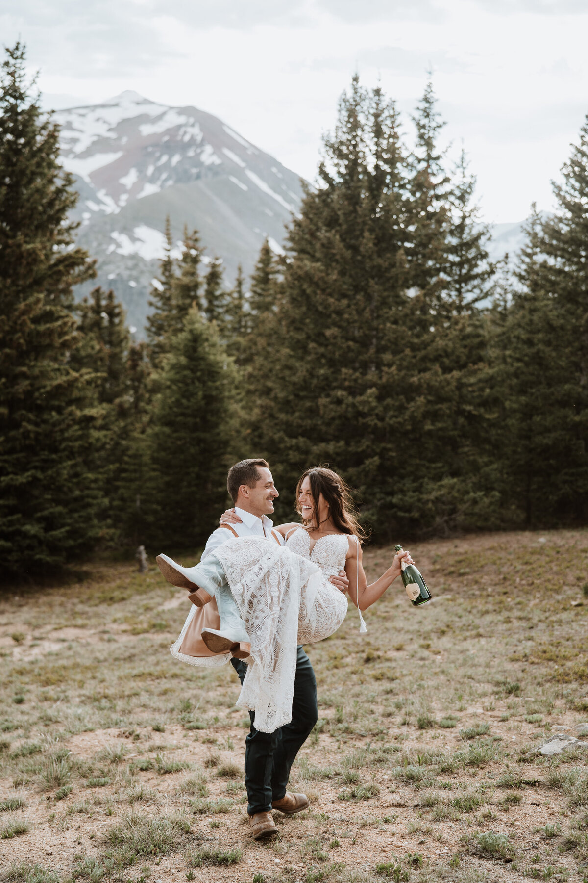 Groom lifting bride with champagne in hand after joyful Hoosier Pass elopement celebration.