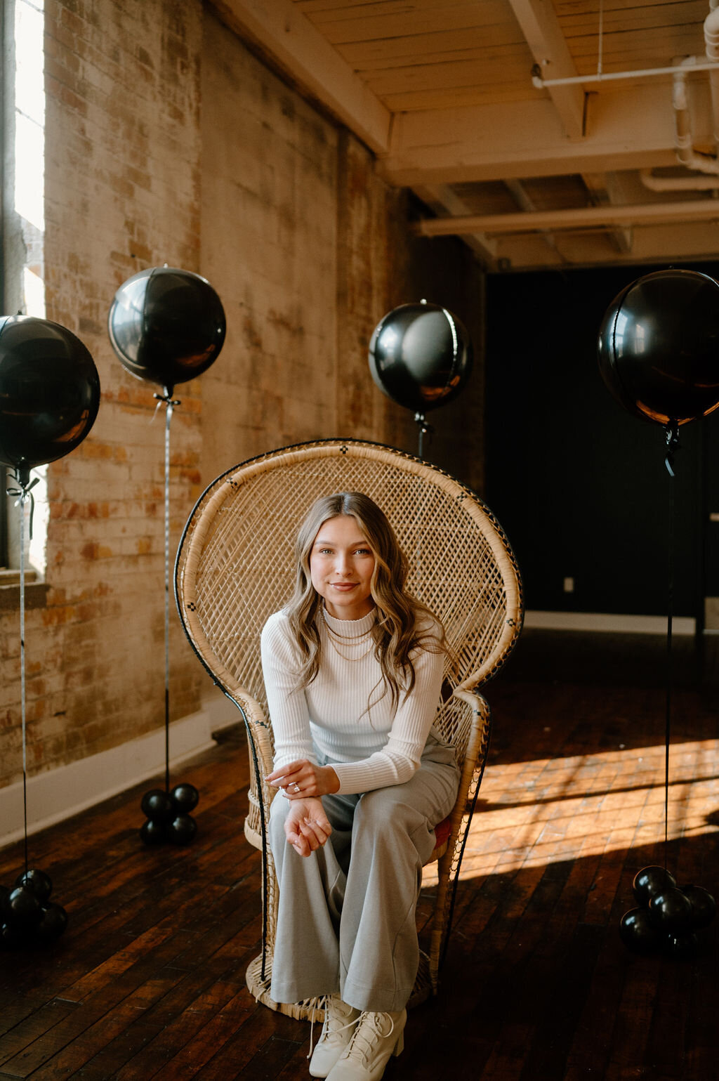 Sandra seated in a wicker chair surrounded by minimalist black balloons, ideal for branding.