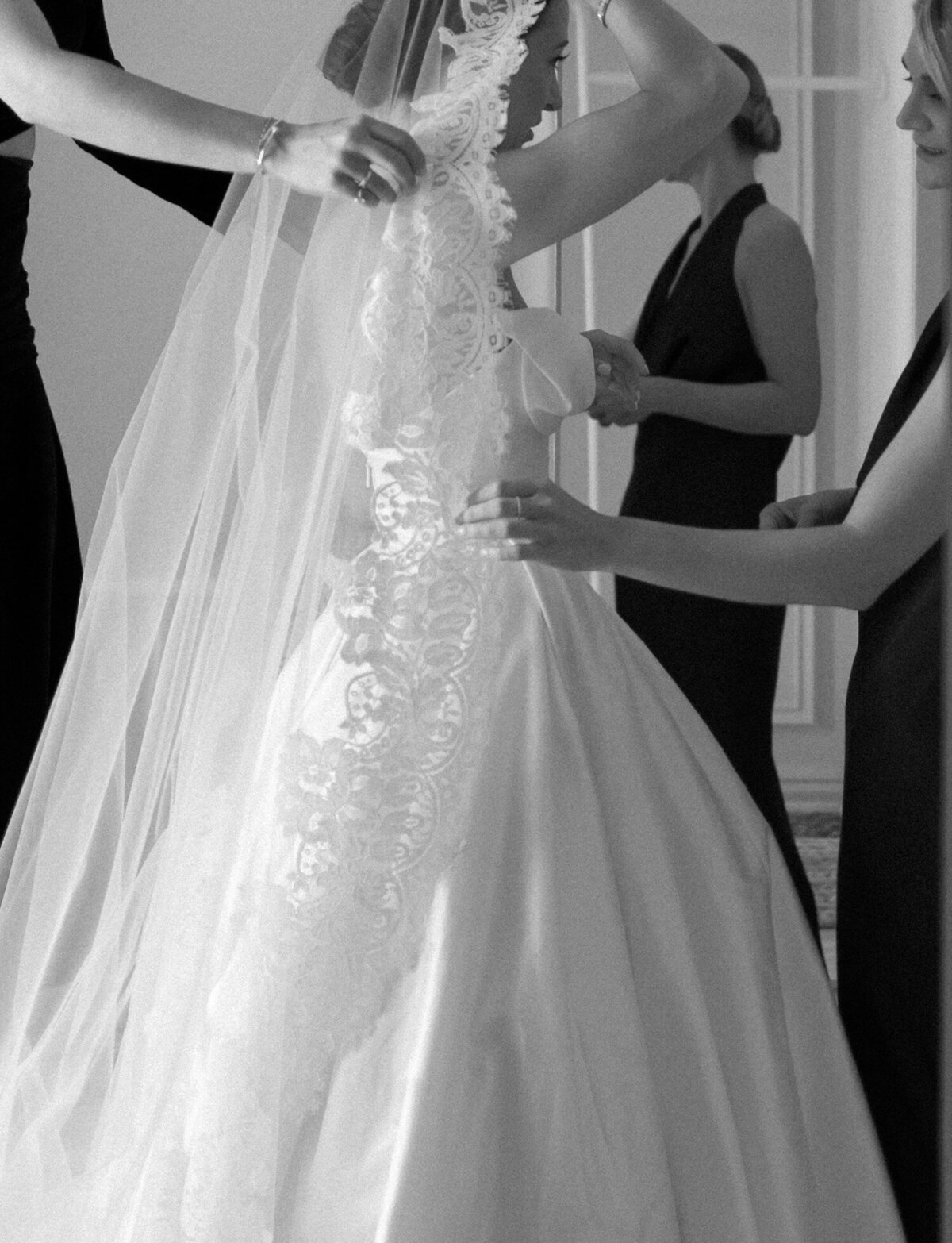 a bride's friends' hands reach to adjust her lace mantilla veil while getting ready for her Detroit wedding at 1 Room Hotel