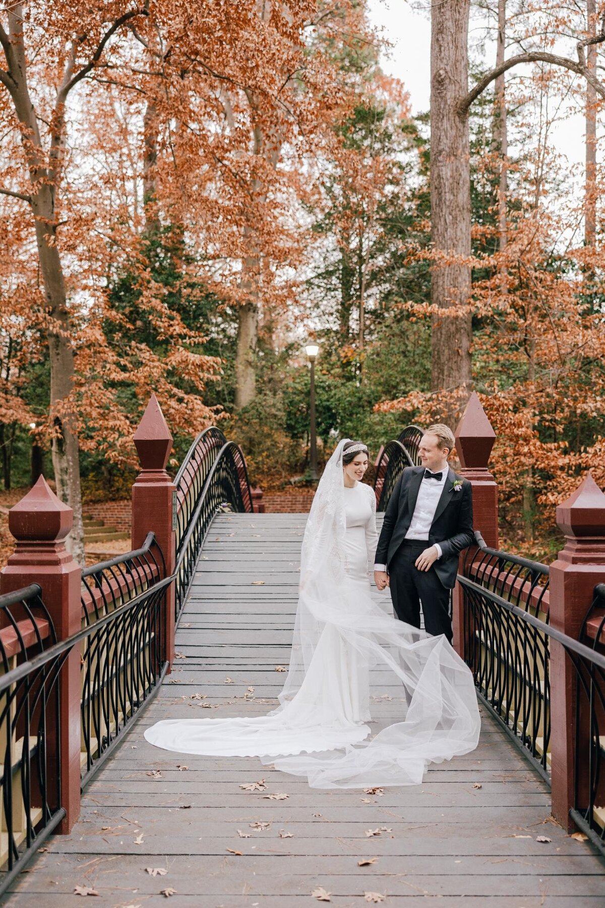 Bride and groom walking across a bridge in an autumnal setting.