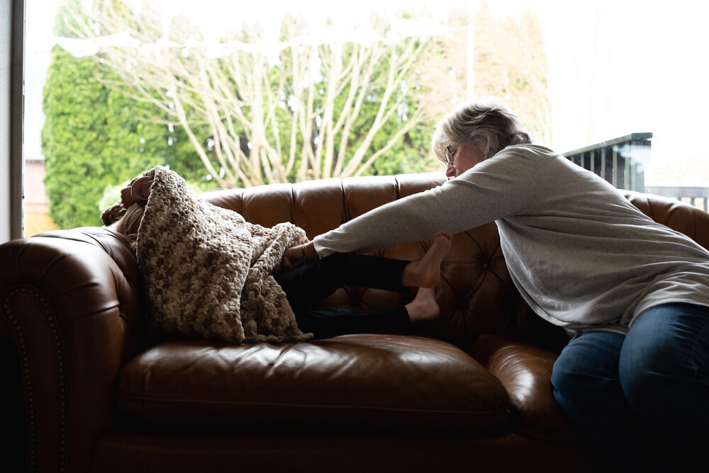 Grandma tickling granddaugther on couch in front of large window