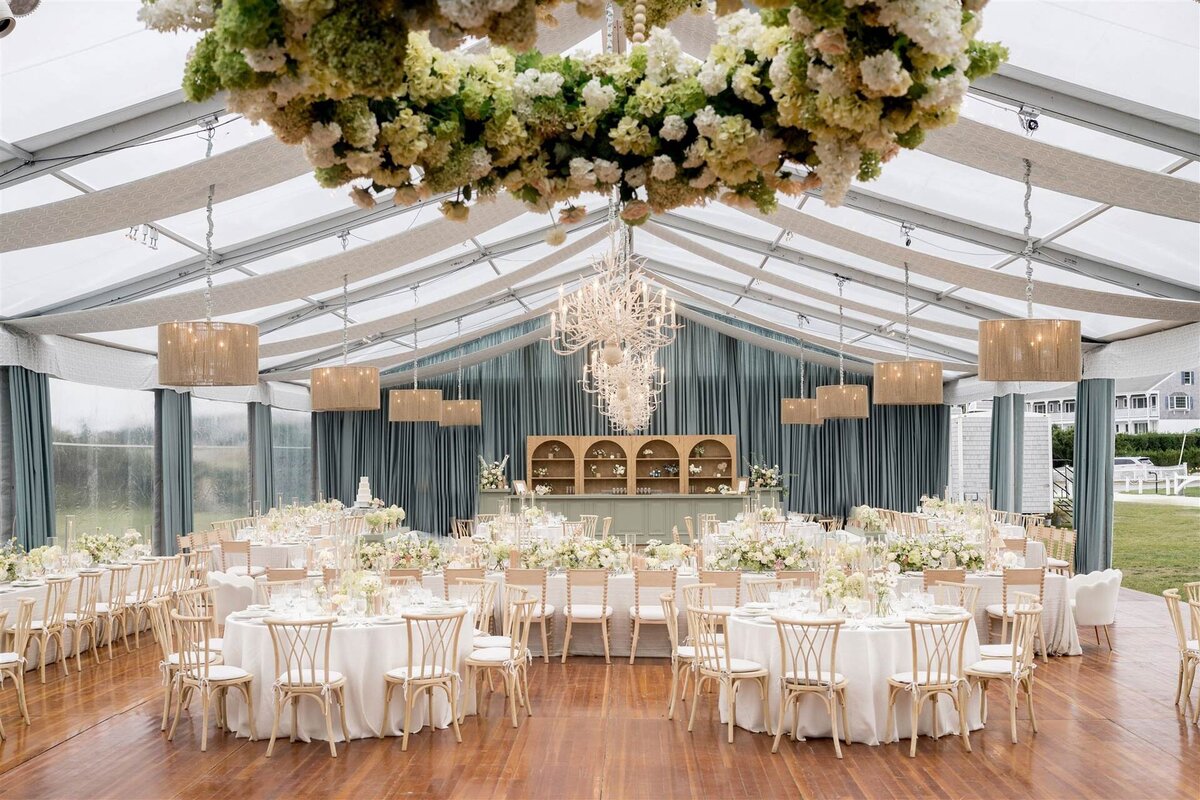 Tented wedding reception with blue drapery, jute chandeliers, white table cloths and natural florals