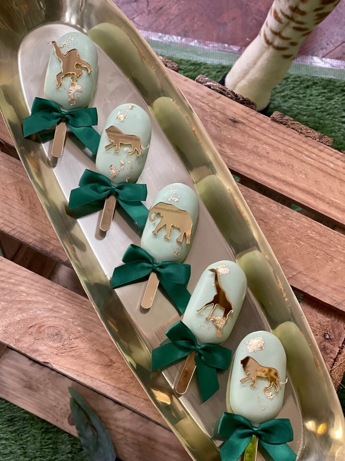 Children's party cake pops with gold animals and green silk ribbon in a gold tray