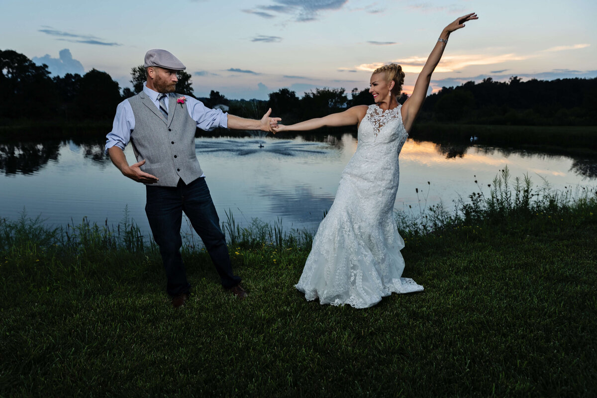 Bride and groom dancing by a pond at sunset